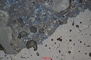  Mikrostruktur eines Magnesiaspinellsteins (unten rechts) mit Korrosion durch Zementklinker (oben links). Die Periklaskristalle sind ein Widerstand gegen Infiltration und Verschleiß, der auf ihre Oberfläche begrenzt ist. Poren (dunklere Flächen) werden durch die Kristalle geschützt und wegen ihrer geschlossenen Art nicht infiltriert 